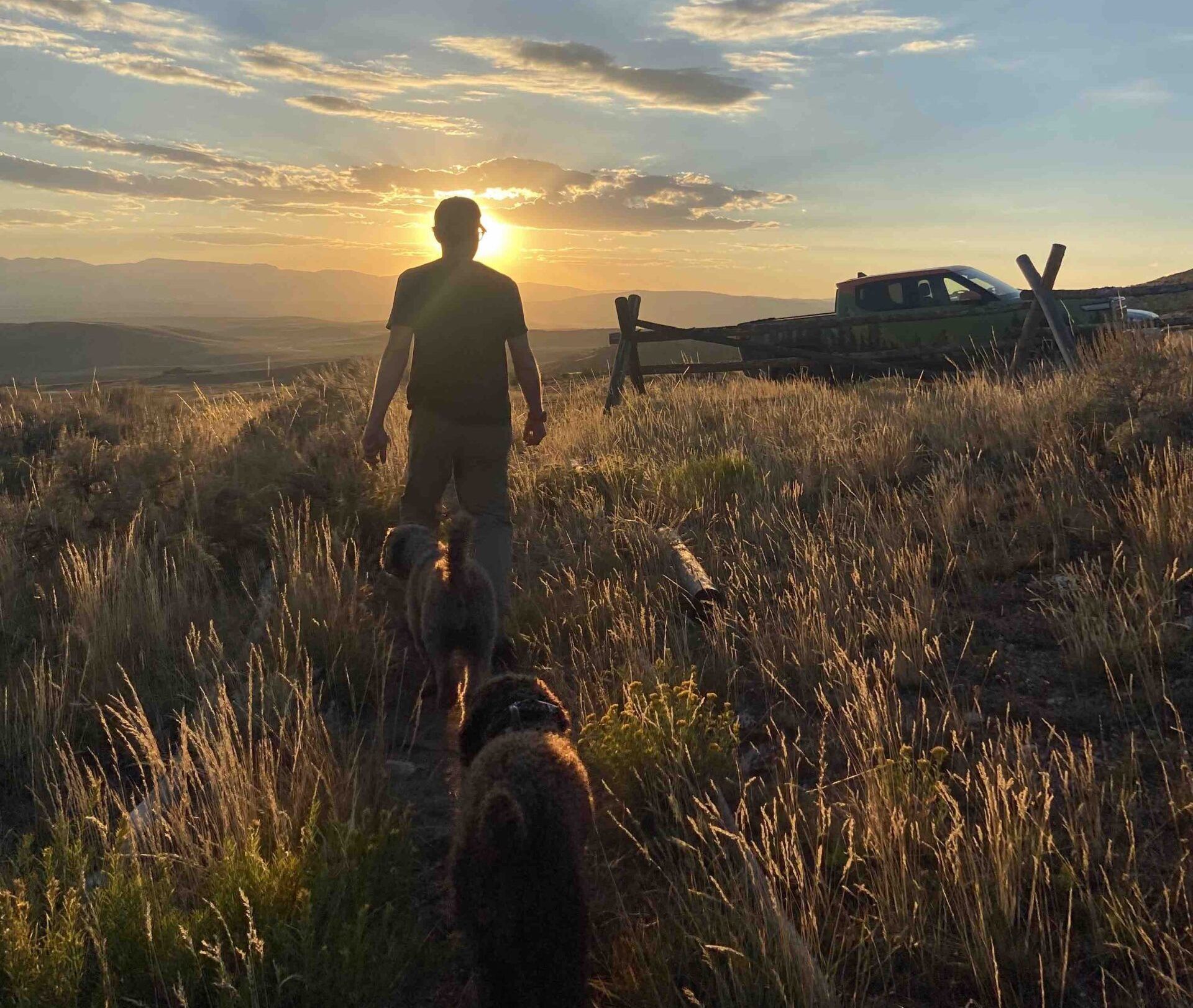 Arthur Morgan in real life, in the mountains, near a Rivian truck, with two dogs following him.